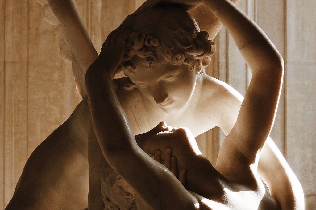 부드러움의 표현으로 서로의 머리를 부드럽게 잡고 있는 두 개의 얽힌 인물을 묘사한 대리석 조각의 클로즈업.