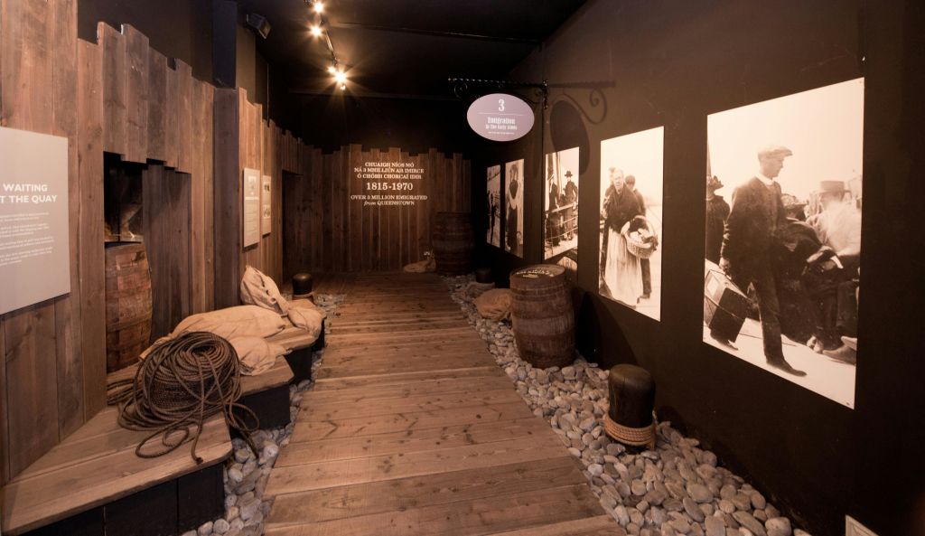 조명이 희미한 전시 공간의 벽에 배럴, 자루 및 역사적인 사진으로 둘러싸인 목조 통로.