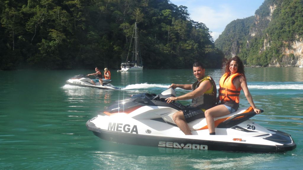 절벽과 녹지를 배경으로 아름다운 만에서 제트 스키를 타는 남녀. 둘 다 미소를 짓고 구명조끼를 입고 있습니다.