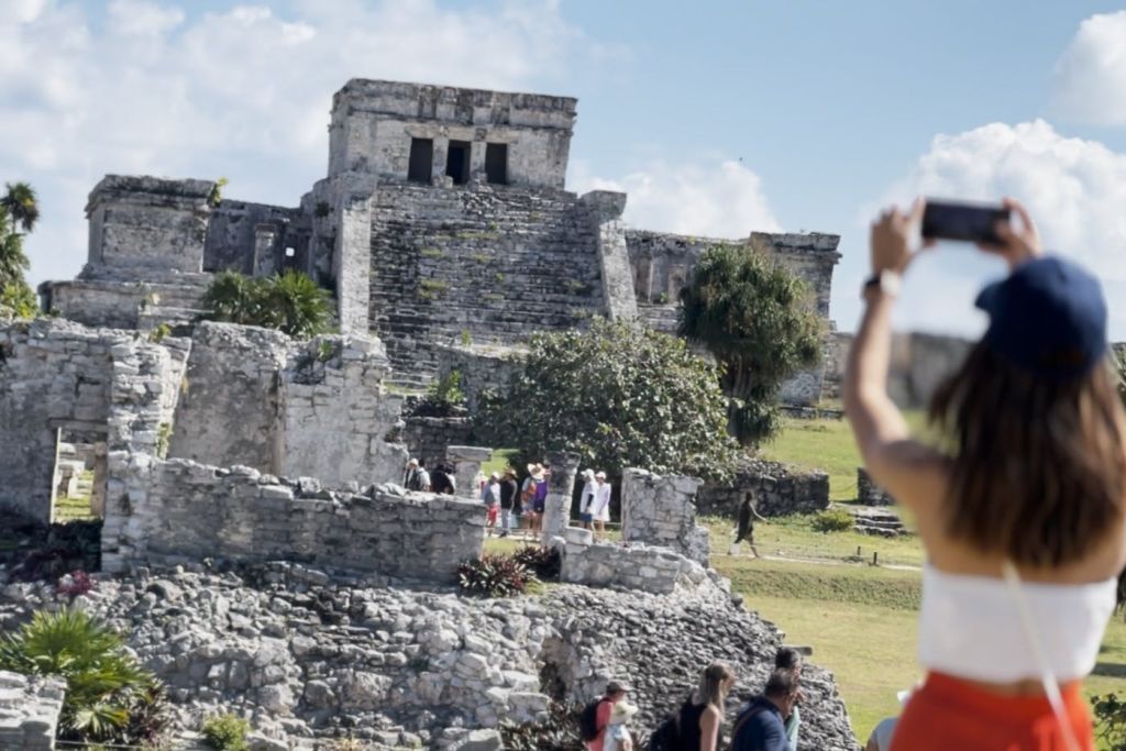 관광객들은 한 사람이 전경에서 사진을 찍으며 맑은 하늘 아래 고대 석조 유적을 탐험합니다.