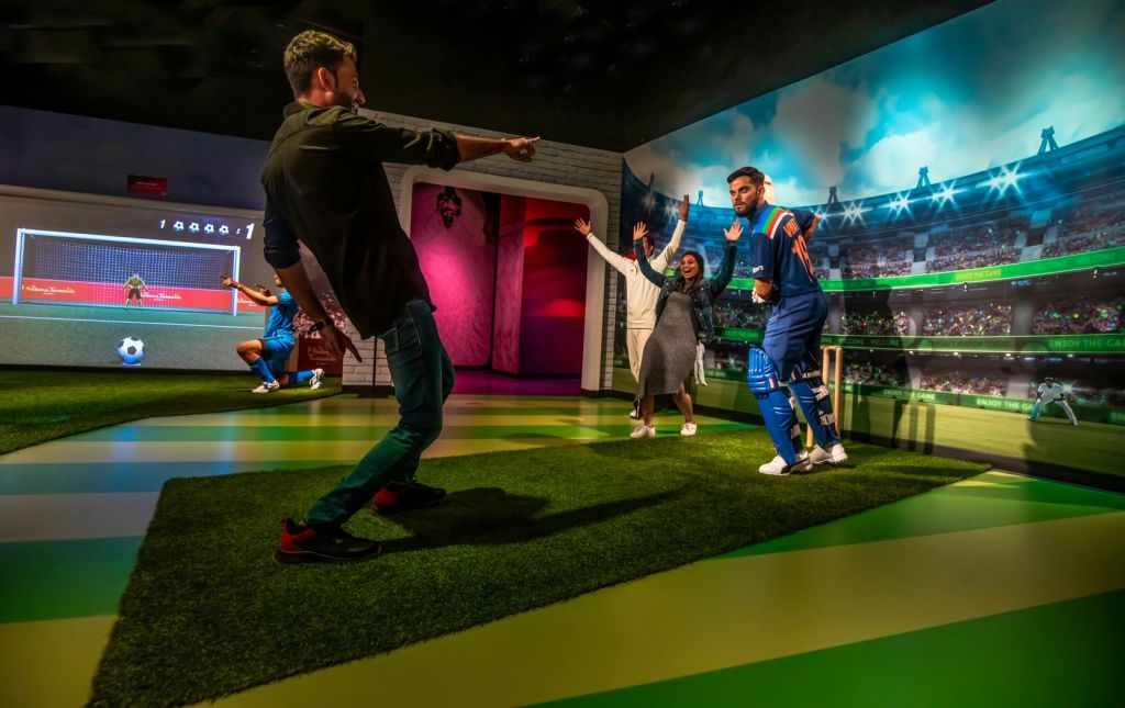 인조 잔디와 경기장을 배경으로 한 경기장을 테마로 한 전시회에서 크리켓 선수의 왁스 피규어를 들고 포즈를 취하는 사람들.