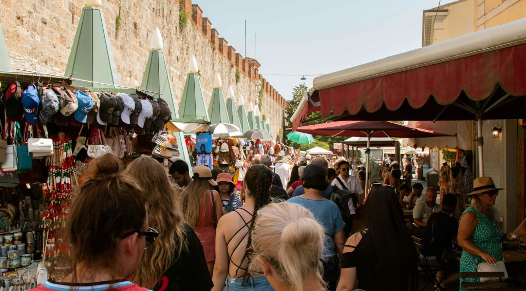오래된 벽돌 벽을 배경으로 노점을 둘러보고 모자, 옷, 액세서리를 파는 사람들로 북적이는 야외 시장.