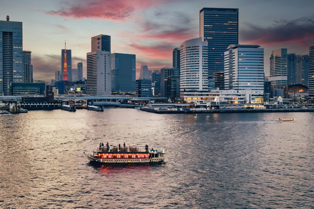 화려한 석양을 배경으로 높은 건물의 도시 풍경을 배경으로 승객이 탑승한 보트가 물속을 활보하고 있습니다.