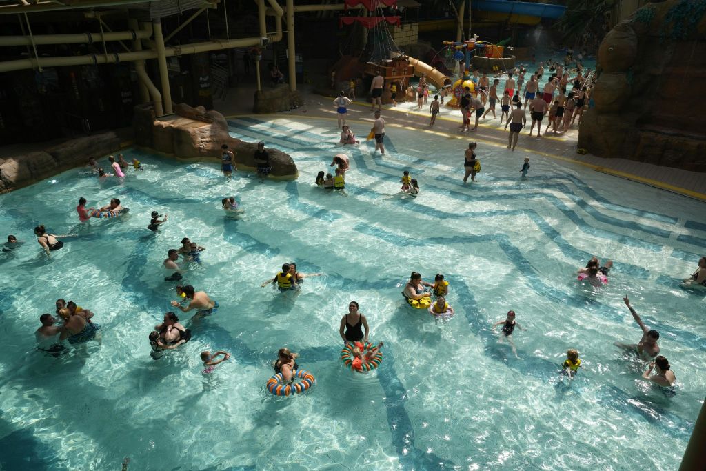 놀이 공간과 파도풀로 둘러싸인 다양한 수레가 있는 대형 실내 워터파크 수영장을 즐기는 사람들.