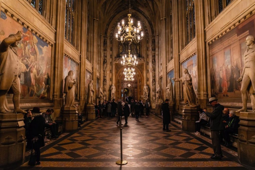 샹들리에, 동상, 벽에 걸린 그림이 있는 화려한 홀 맨 끝에 사람들이 모였습니다.