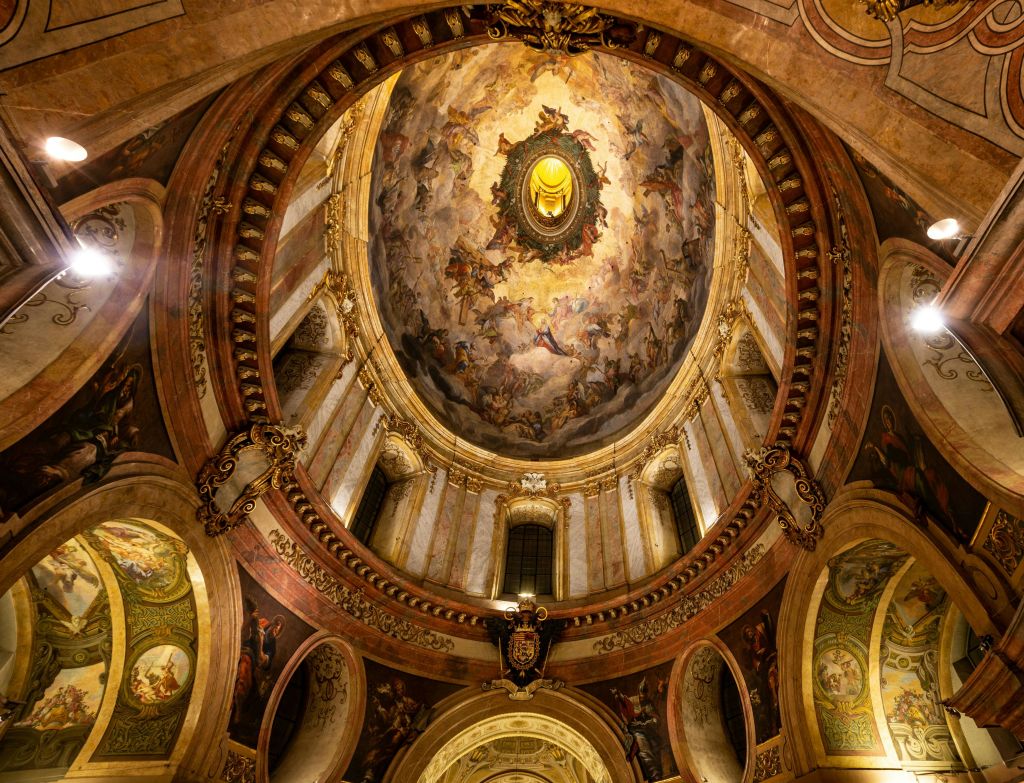 정교한 프레스코화, 금색 액센트, 아치형 창문, 빛나는 얼굴을 형상화한 중앙 메달로 장식된 돔형 천장.