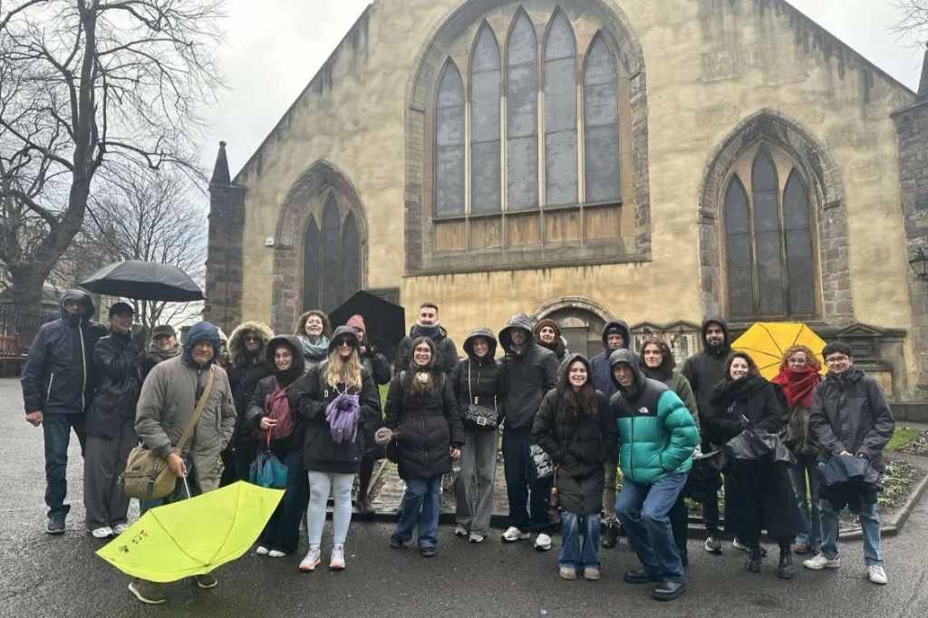 흐린 날 높은 아치형 창문이 있는 석조 건물 앞에 따뜻한 옷을 입은 한 무리의 사람들이 서 있습니다.