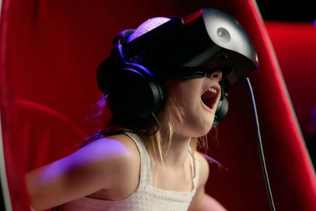 가상 현실 헤드셋과 헤드폰을 착용하고 흥분한 표정을 짓고 빨간색 배경에 앉아 있는 아이.