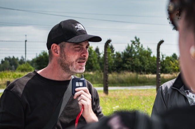 녹음이 우거진 검은색 모자와 셔츠를 입고 울타리를 배경으로 야외에서 워키토키를 들고 있는 남성.