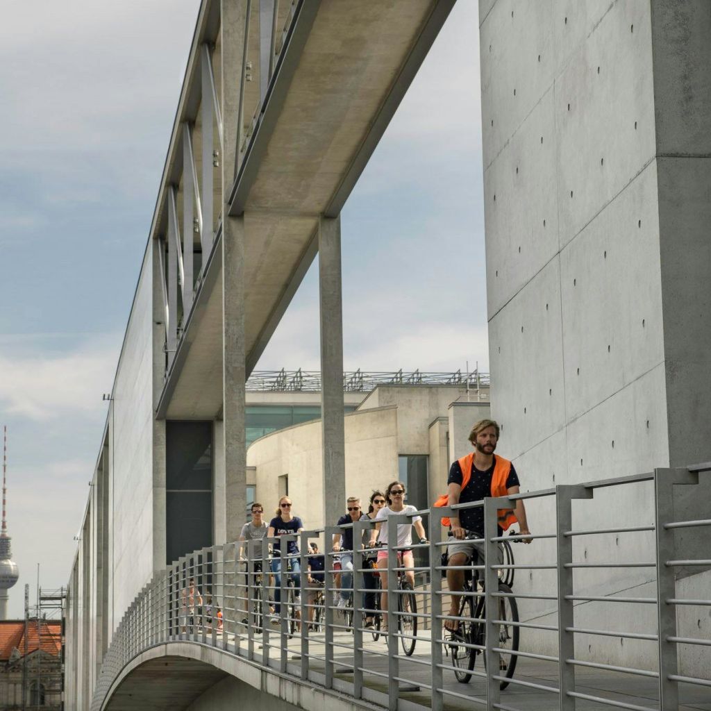 사람들이 자전거를 타고 콘크리트 벽과 난간이 있는 현대적인 보행자 다리를 따라 걷고 있습니다.