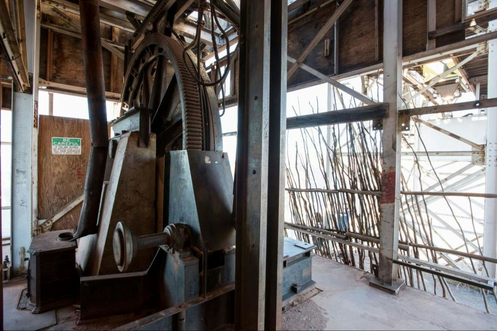 금속 구조물로 둘러싸인 대형 기어와 기계가 있는 산업 환경으로 야외 나무 장벽의 전망을 감상할 수 있습니다.