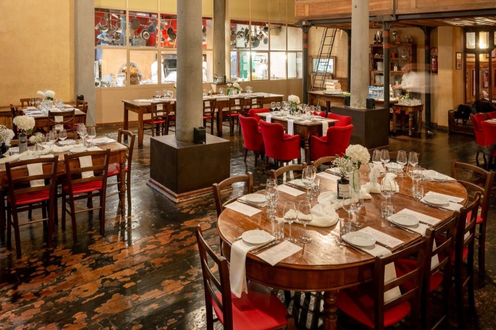 식사가 가능한 나무 테이블, 빨간색 의자, 주방을 향한 커다란 창문이 있는 촛불이 켜진 레스토랑. 하얀 꽃 센터피스가 테이블을 장식합니다.