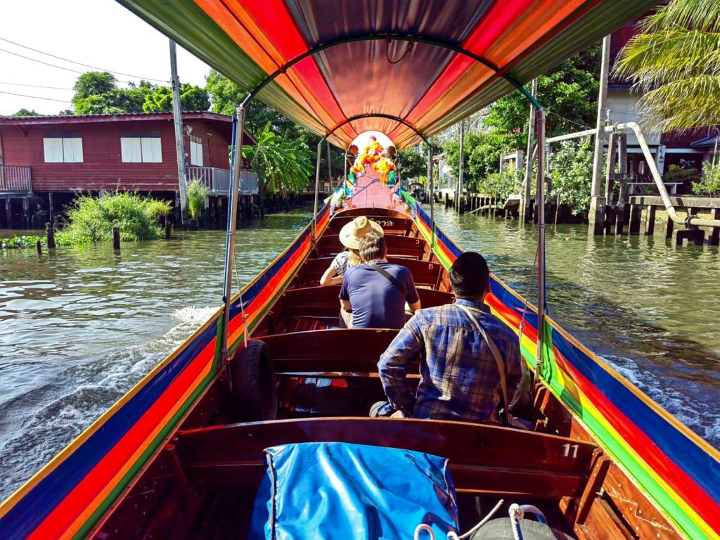 수변 주택과 녹지가 양쪽으로 펼쳐진 운하를 여행하는 다채로운 색상의 보트에 앉아 있는 사람들.