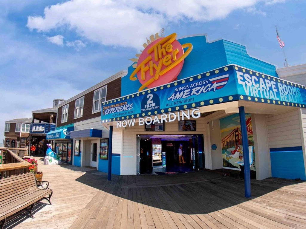 대형 "The Flyer" 표지판과 "Now Boarding" 배너가 있는 보드워크의 야외 놀이 기구 입구.