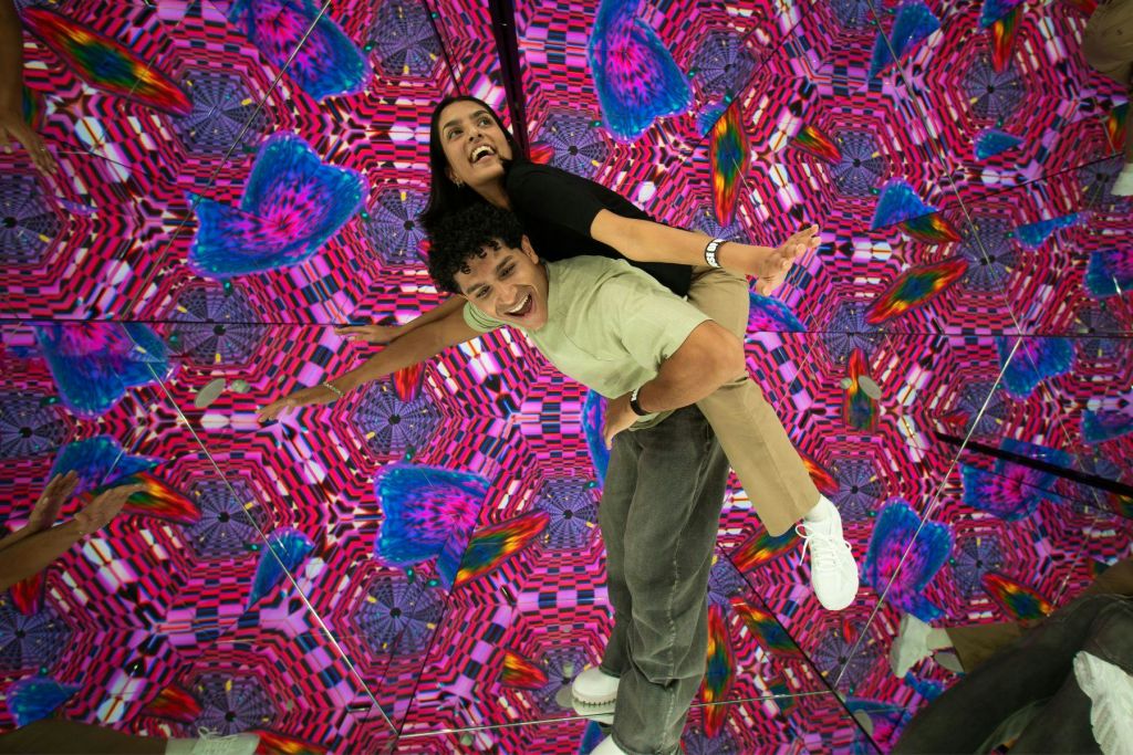 화려한 패턴과 모양을 가진 활기찬 만화경 배경 앞에서 장난스럽게 포즈를 취하는 두 사람.