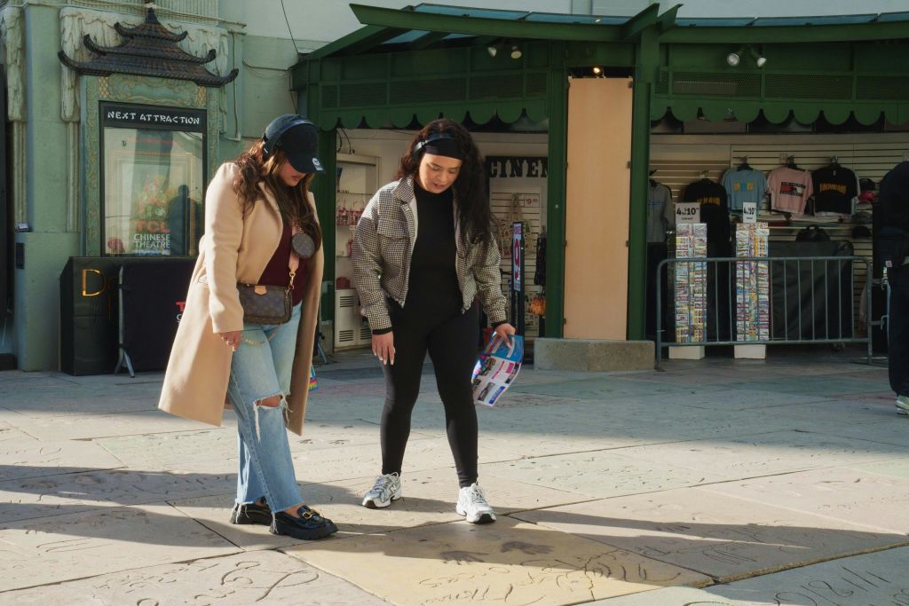 야외에서 포장 도로의 별판을 바라보는 두 명의 여성이 녹색 외관이 있는 상점가 근처에 서 있습니다.