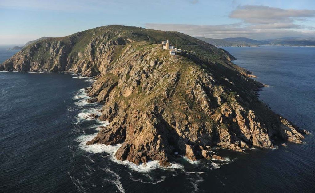 파도가 치는 바위 해안선과 바다로 이어지는 언덕이 많은 산책로에 자리한 등대.