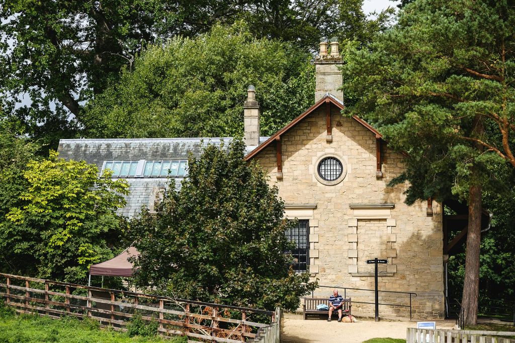 화창한 날 나무와 녹지로 둘러싸인 석조 건물 바깥 벤치에 한 남성이 앉아 있습니다.