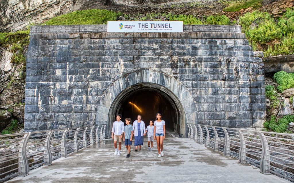입구 위에 'The Tunnel' 과 'Niagara Parks' 라는 표지판이 있는 석조 터널을 걸어 나가는 사람들.