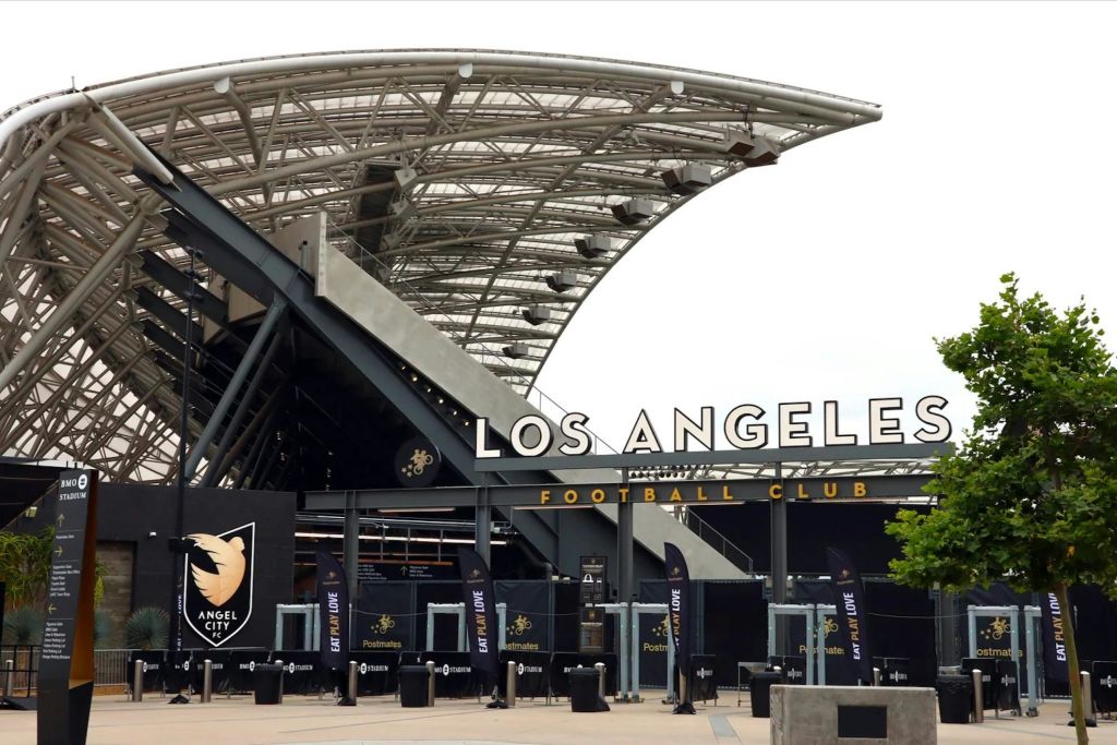 "로스앤젤레스 축구 클럽" 표지판과 지붕이 있는 구조물이 있는 경기장 입구. Angel City FC 로고와 배너가 표시됩니다.