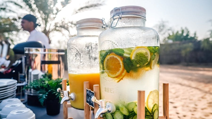 레모네이드 항아리와 오렌지 주스, 접시, 컵, 흐릿한 셰프가 배경으로 놓인 야외 뷔페 테이블.