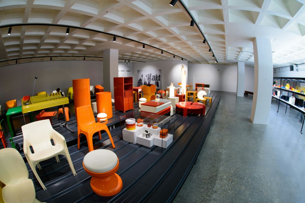 갤러리 내 검은색 플랫폼에 다양한 주황색 및 흰색 플라스틱 가구가 전시된 현대 미술 전시회입니다.
