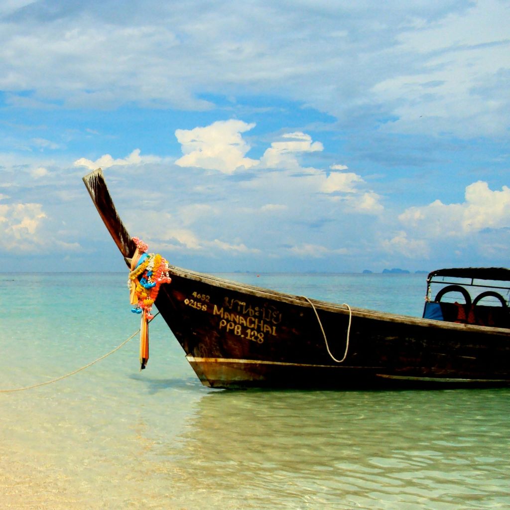 잔잔하고 맑은 바다를 배경으로 부분적으로 흐린 하늘을 배경으로 나무 보트가 해안에 묶여 있습니다.