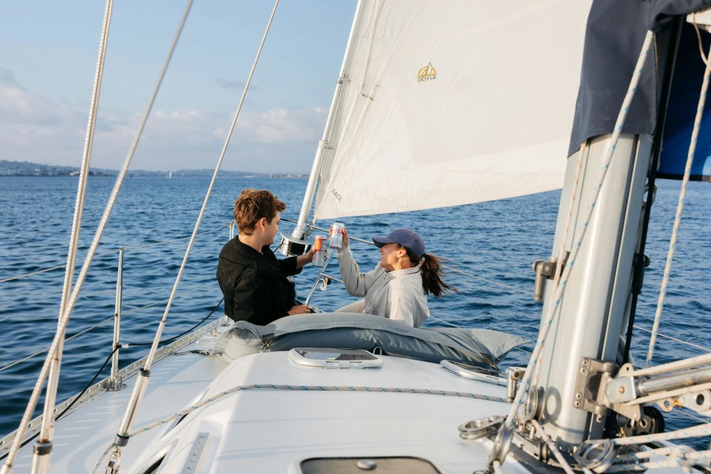 돛을 올리고 돛단배의 활에 앉아 건배를 하며 음료를 올리는 젊은 부부