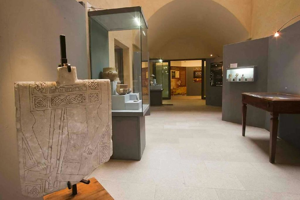 아치형 천장이 있는 방의 유리 케이스에 돌 조각과 유물이 전시된 박물관 전시관입니다.