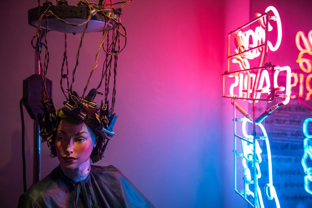 화려한 분홍색과 파란색 조명이 비추는 빈티지 미용 장치 아래 전선에 헤어 컬러가 부착된 마네킹입니다.