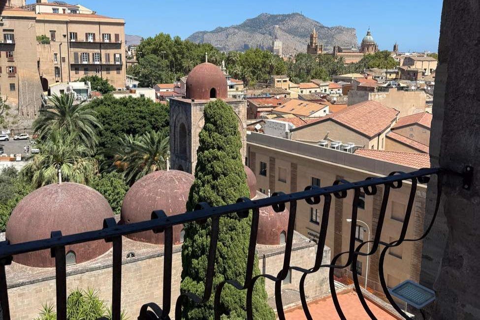 붉은 돔 건물, 울창한 녹지, 맑고 푸른 하늘 아래 먼 산이 있는 도시가 내려다보이는 발코니에서 바라보는 전망.