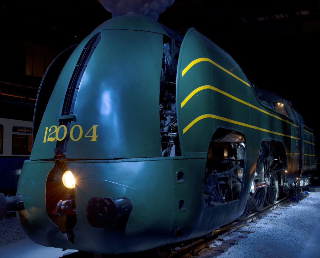 노란색 줄무늬가 있는 녹색 빈티지 증기 기관차와 헤드라이트로 비춰진 12004라는 숫자가 실내에 전시되어 있습니다.