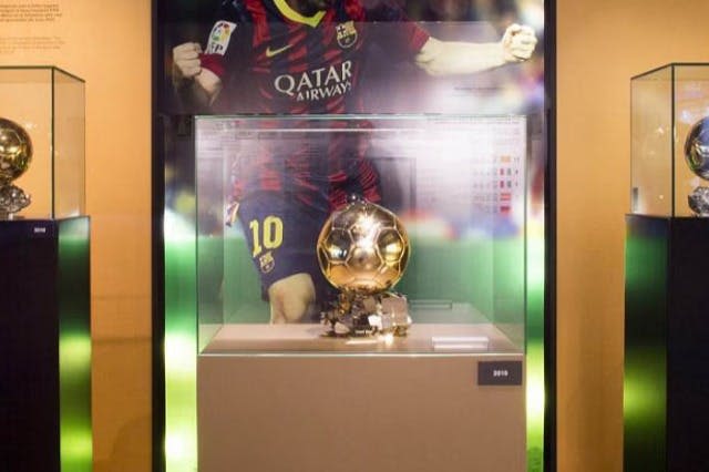 빨간색과 파란색 유니폼을 입은 축구 선수의 사진이 배경으로 유리 케이스에 표시된 황금색 축구 트로피입니다.