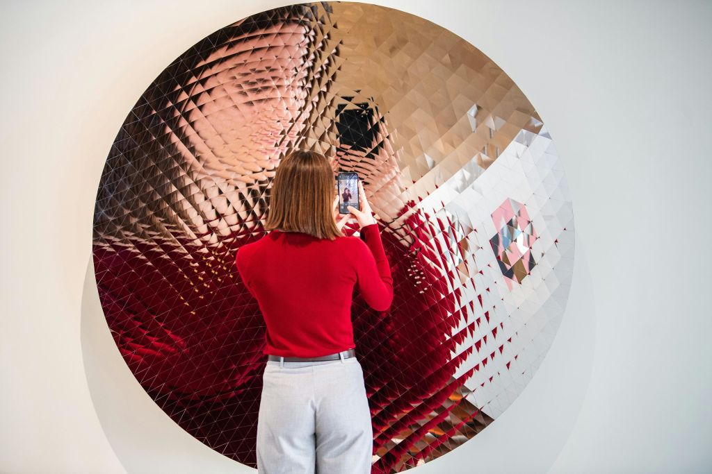 빨간 스웨터를 입은 사람이 기하학적 패턴의 커다란 질감의 원형 거울로 자신의 모습을 촬영합니다.
