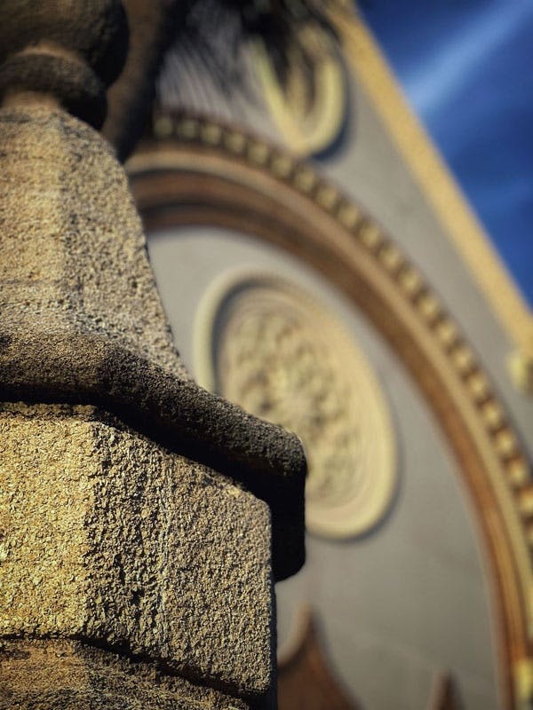 배경의 건물 위에 흐릿한 화려한 시계 얼굴로 초점이 맞춰진 돌기둥의 클로즈업.