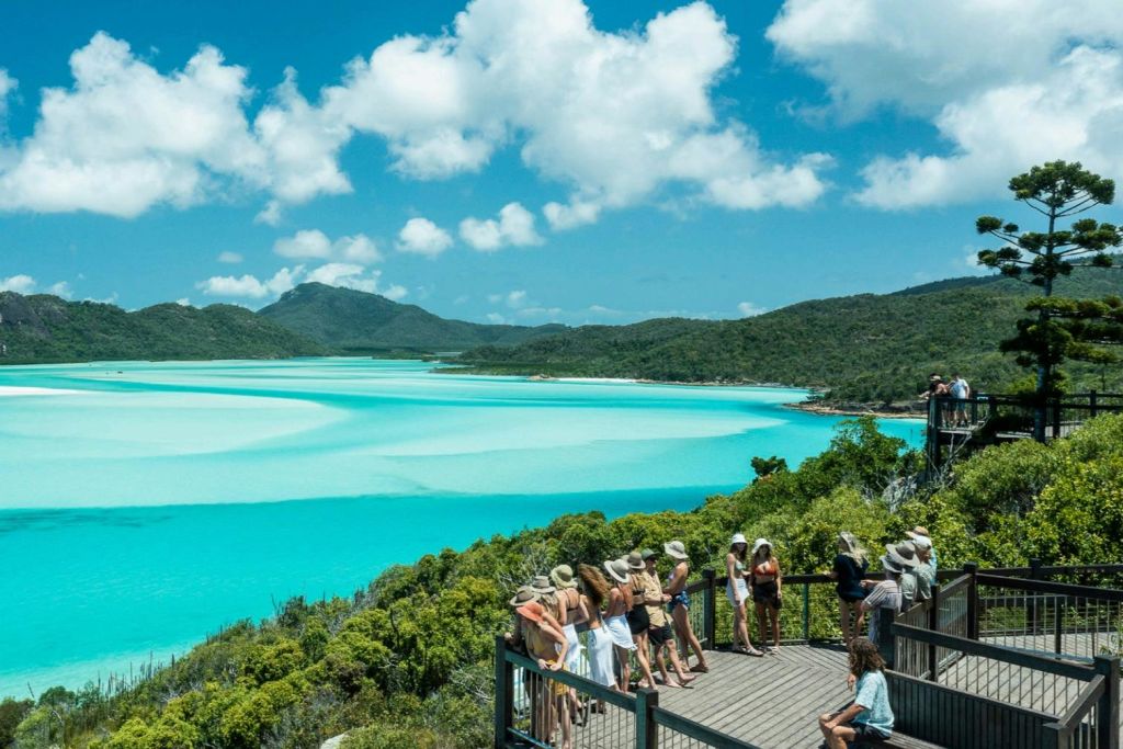 푸른 녹음과 부분적으로 흐린 하늘 아래 언덕으로 둘러싸인 경치 좋은 청록색 만이 내려다보이는 전망대에 앉아 있는 사람들의 일행.