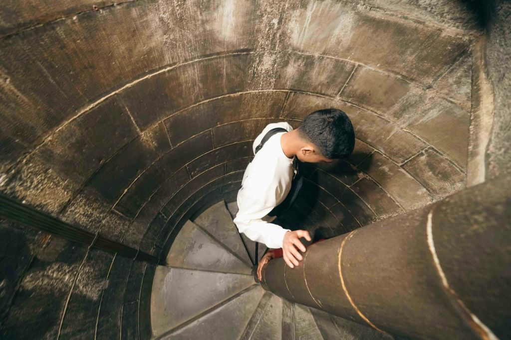돌로 만든 좁은 나선형 계단을 내려오는 사람이 중앙 기둥을 잡고 지지합니다.