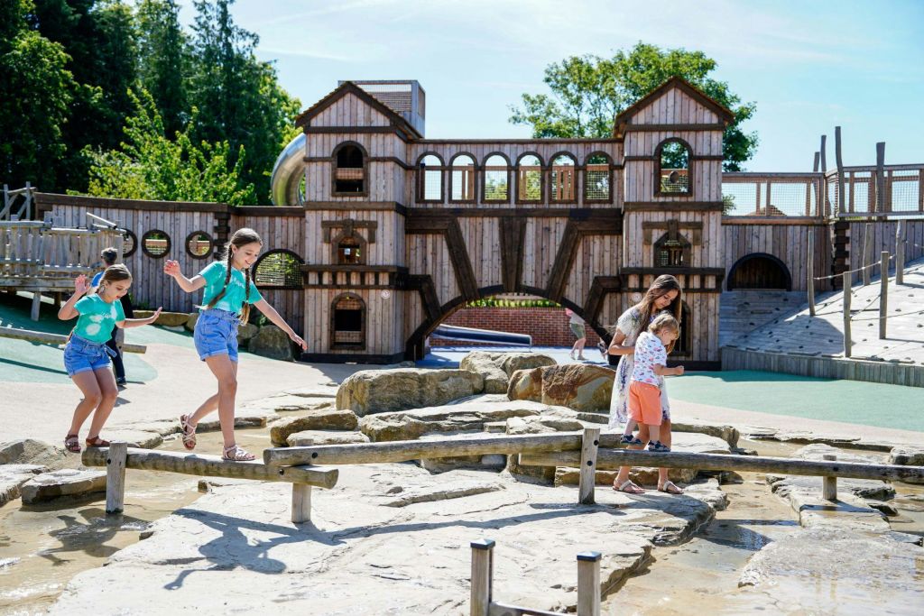 커다란 나무 놀이 구조를 배경으로 놀이터에서 나무 기둥에 균형을 맞추는 두 소녀.