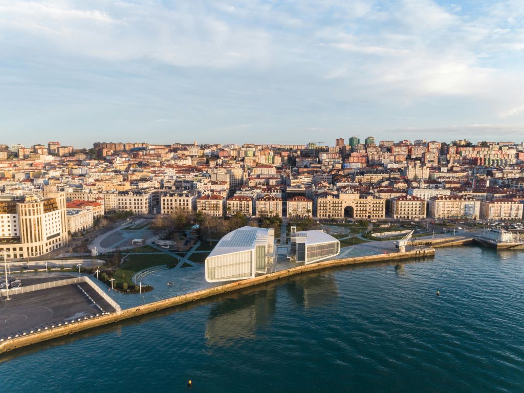 해안가를 따라 자리한 현대적인 흰색 건물, 빽빽한 도심 지역, 맑은 물이 어우러진 해안 도시의 공중 전망.