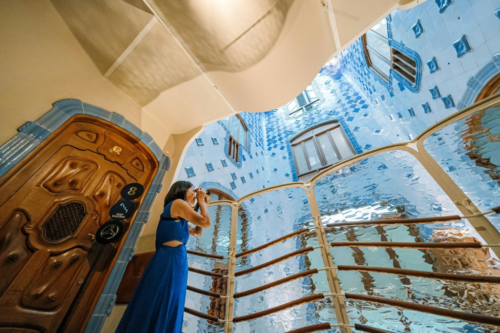 파란색 드레스를 입은 사람이 곡선과 나무 디테일이 있는 건물의 화려한 파란색 타일 내부를 촬영합니다.