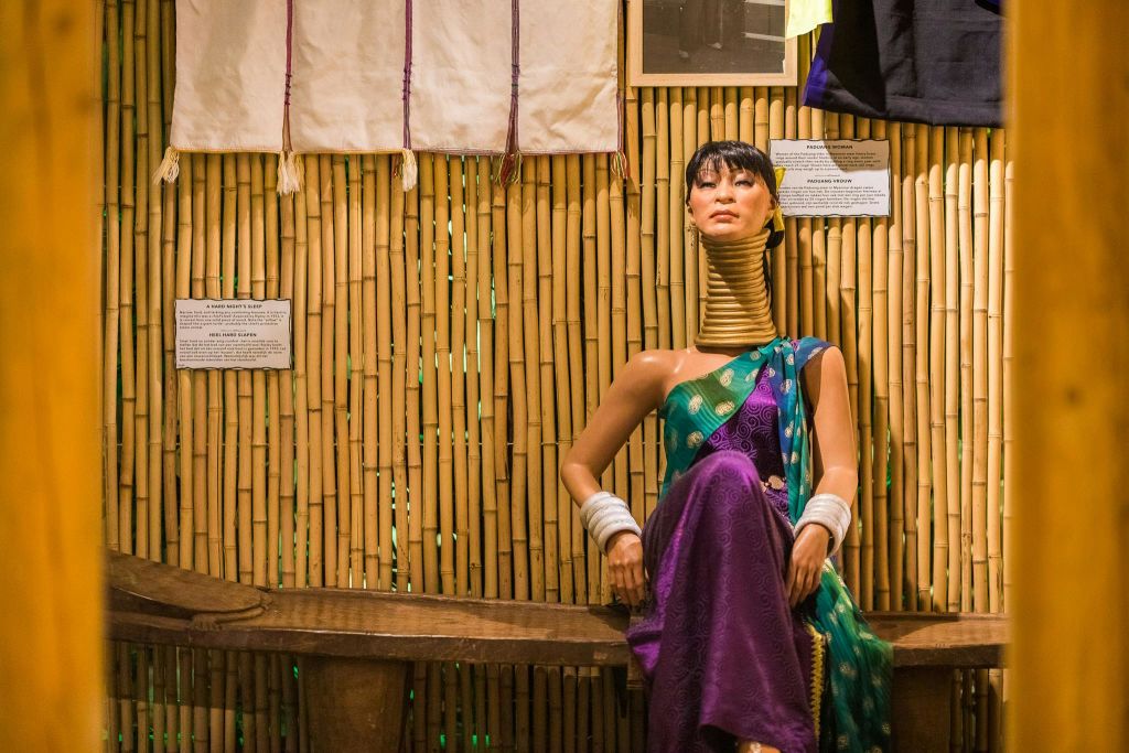 목걸이와 전통 복장을 한 마네킹이 대나무 벽 앞 벤치에 걸려 있습니다.