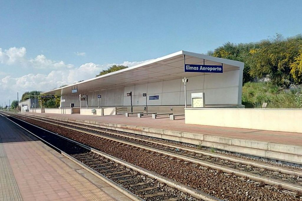 맑은 하늘 아래 벤치, 표지판, 빈 선로가 있는 '엘마스 아에로포르토' 라는 이름의 야외 열차 플랫폼.