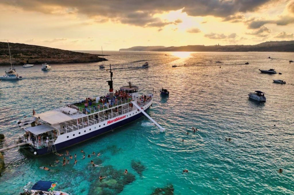 해질녘 석양과 멀리 떨어진 땅을 배경으로 청록빛 바다에서 수영을 즐기는 '혼블로어 (Hornblower)' 라는 이름의 보트.