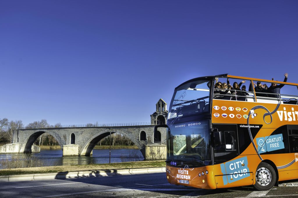 맑은 날 강을 건너는 유서 깊은 석조 다리와 함께 "비지트 아비뇽 (Visite Avignon)" 이 있는 2층 투어 버스.