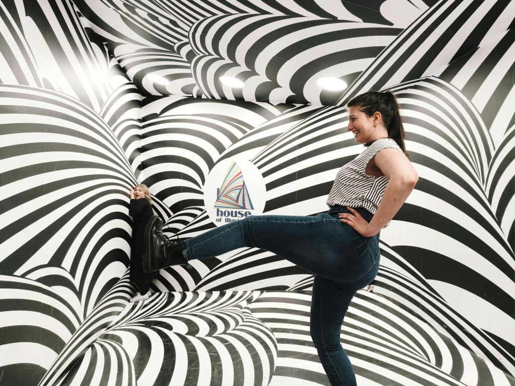 벽과 바닥에 흑백 소용돌이 무늬가 있는 방에서 한 여성이 장난스럽게 포즈를 취하고 있습니다.