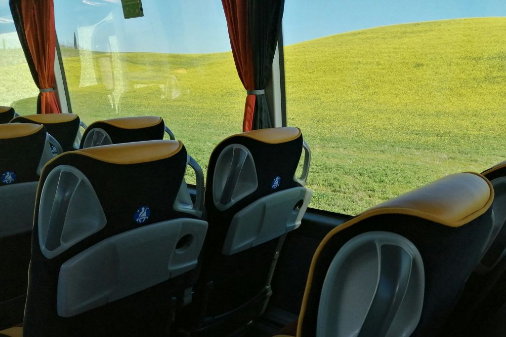 빈 좌석이 보이는 버스 내부와 바깥에 초록색과 노란색 잔디가 깔린 언덕이 보이는 창문에서 바라보는 전망.