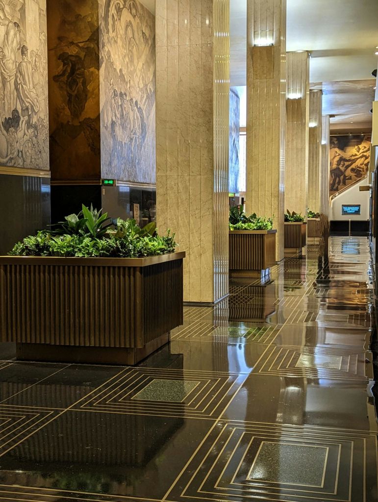 벽화와 건축 디테일이 돋보이는 대형 화분, 장식용 벽, 반사 타일 바닥이 있는 세련된 로비입니다.