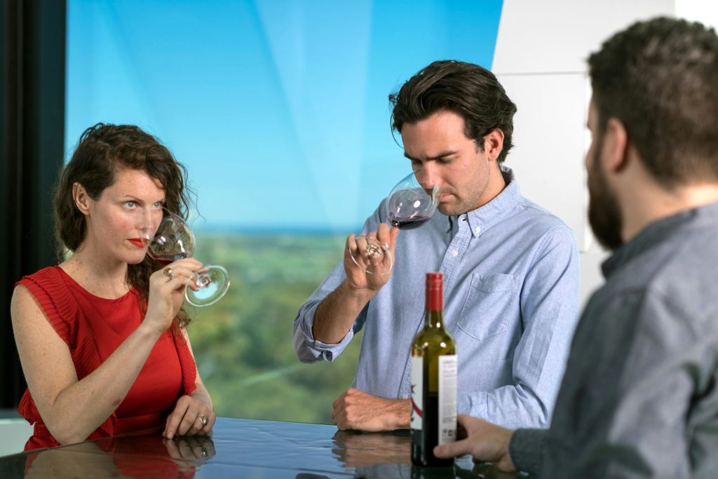 한 남성과 한 여성이 카운터에서 와인 한 병을 곁들인 레드 와인을 시음하고 있습니다. 창문으로 아름다운 풍경이 보입니다.