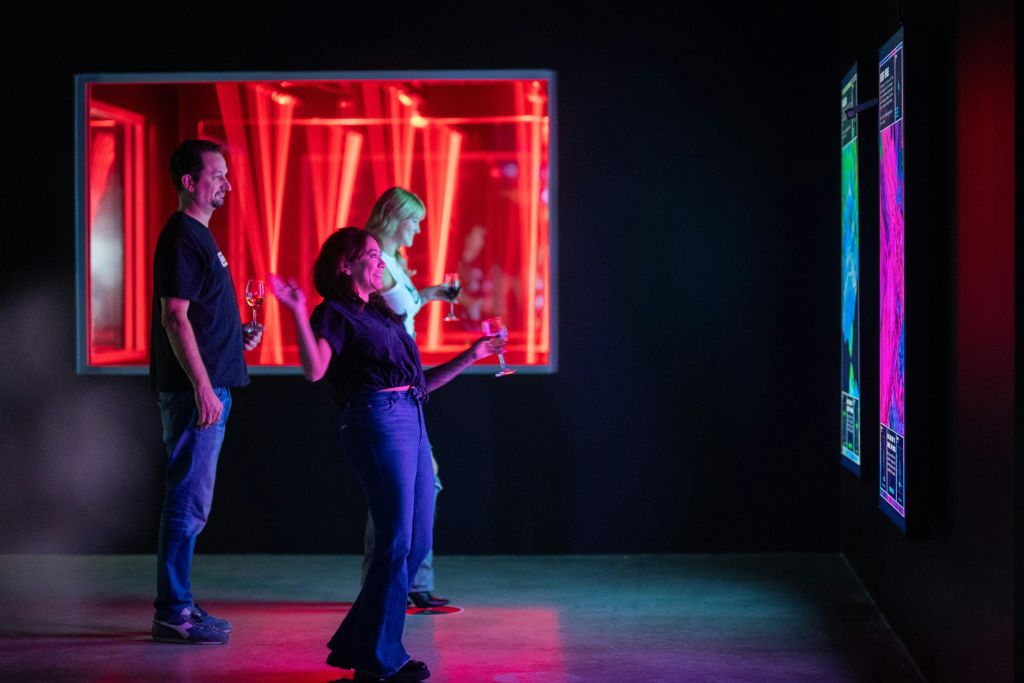 사람들은 어두운 방에서 디지털 디스플레이와 상호 작용하며 배경에 빨간색 조명이 보입니다.