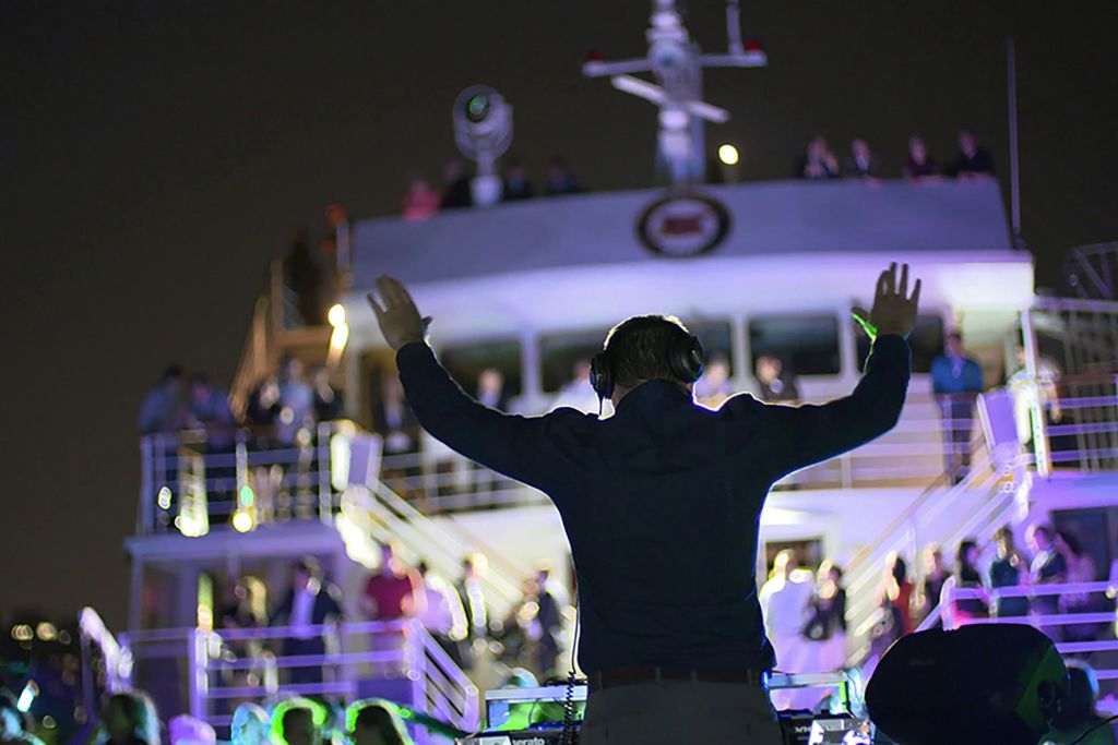 밤에는 DJ가 배 위에서 공연을 펼치며, 많은 사람들이 갑판에서 음악과 조명을 즐기고 있습니다.